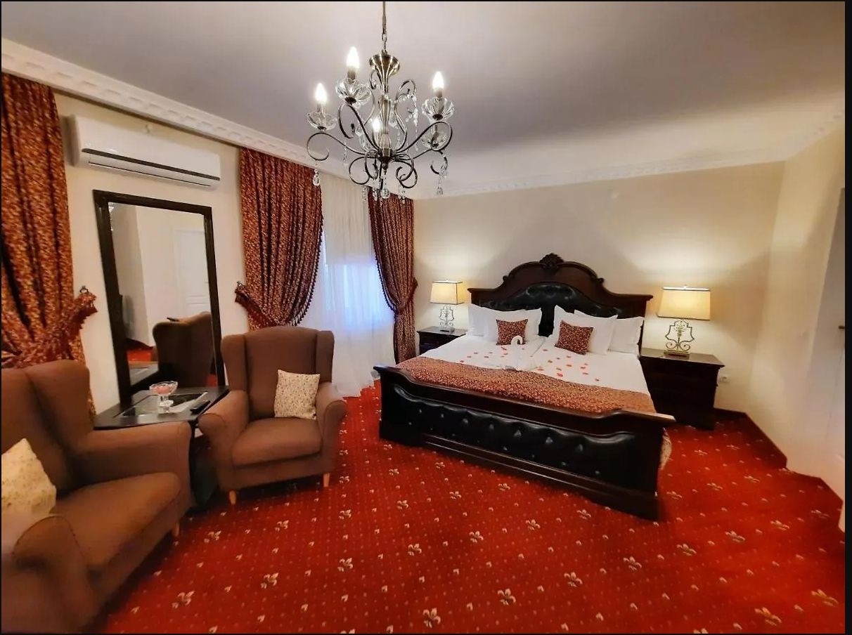 Cameră Deluxe cu candelabru, mobilier din lemn închis și textile vișinii
